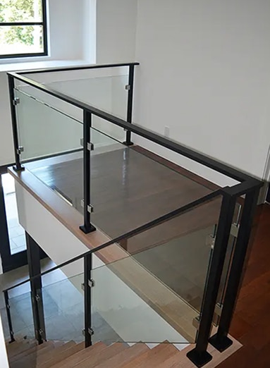 Escalier moderne avec garde-corps en verre et poteaux/rampe en métal noir. Marches et palier en bois clair.